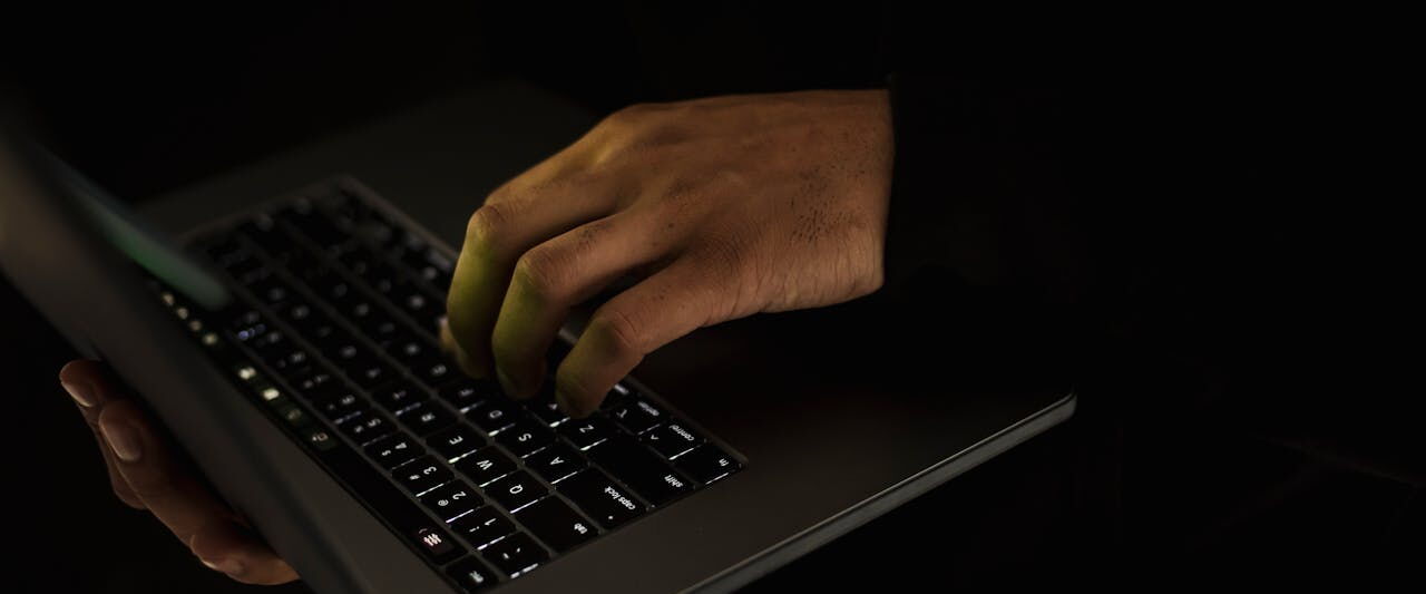 A single hand typing on a laptop keyboard in a darkened room.
