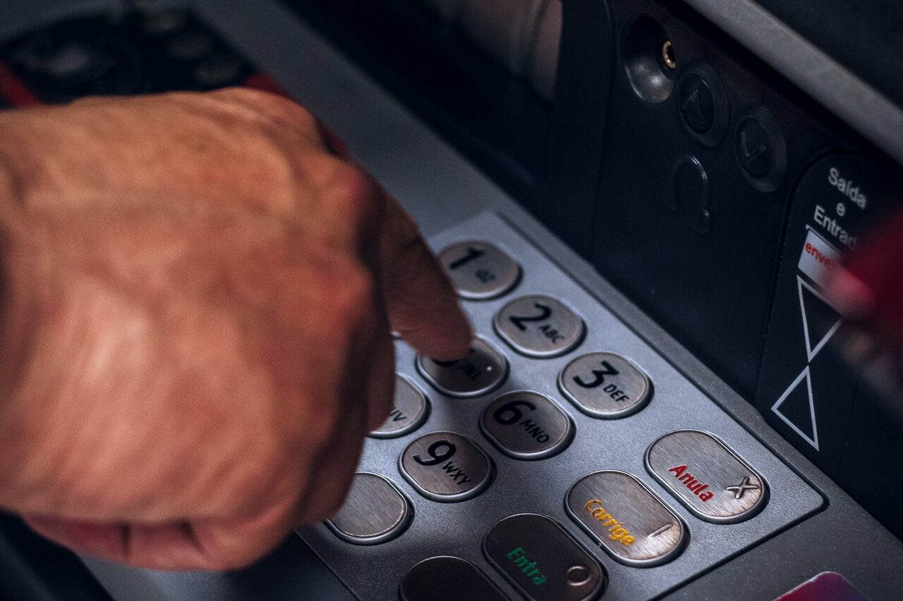 A hand entering a PIN on the keypad of a cash machine.