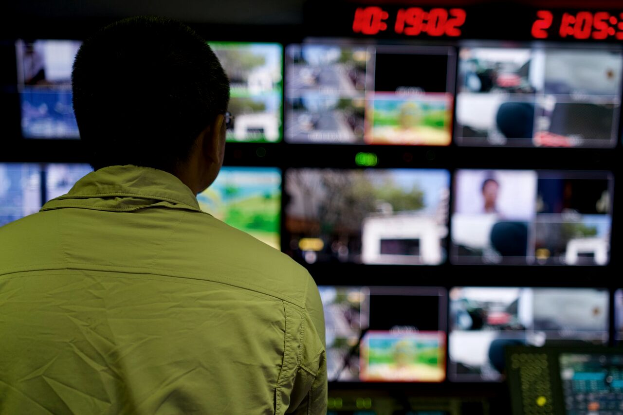 An analyst standing before a wall of monitors showing many live feeds at once.