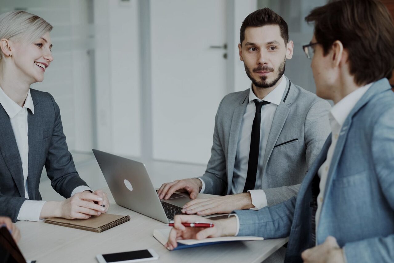 Three colleagues talking over a laptop at an office table.