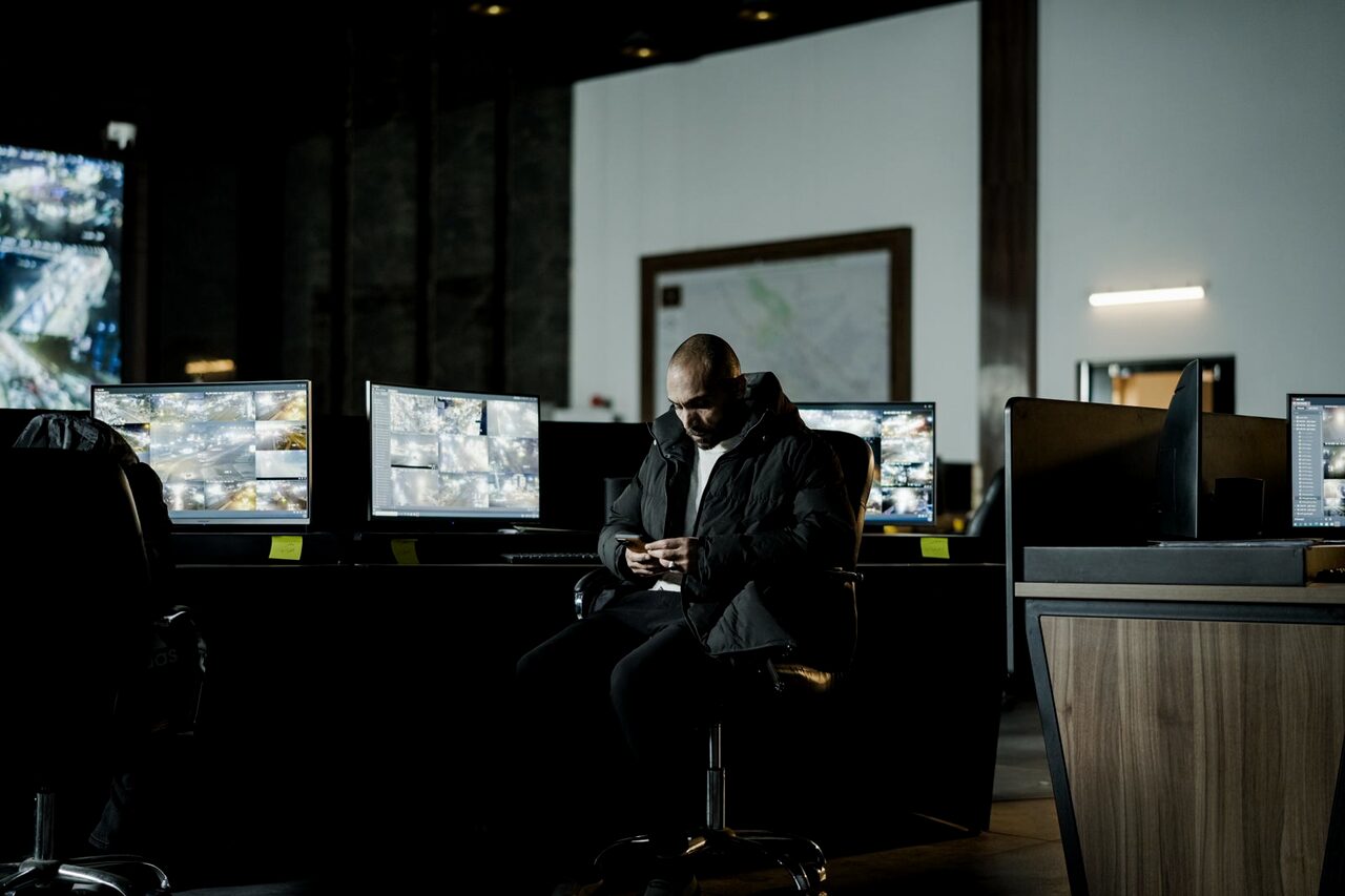 A security officer monitoring incident feeds across several screens in a dark operations centre.