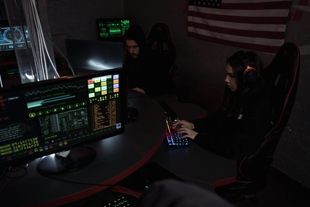 A security operator at a workstation lit by the red glow of dashboards showing user-activity data.