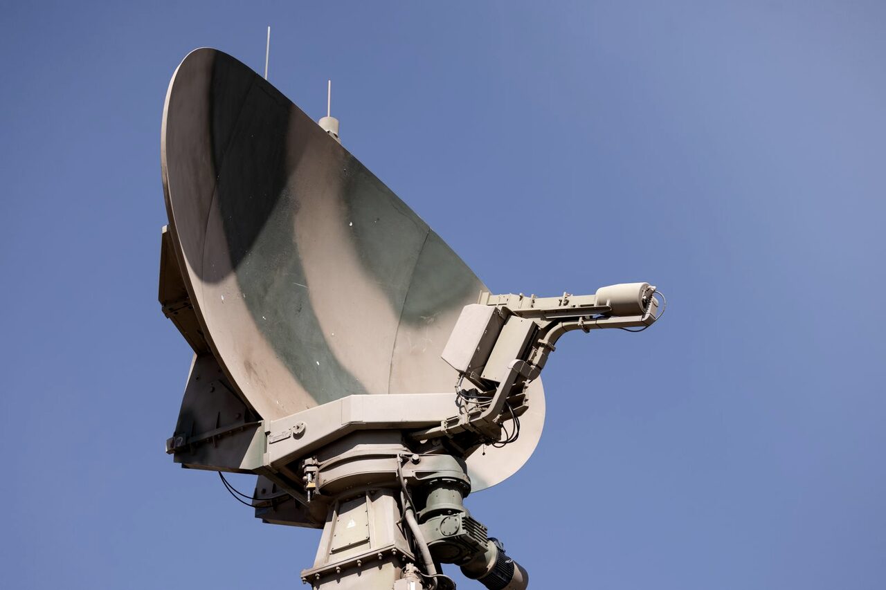 A military radar array turning against a clear blue sky.