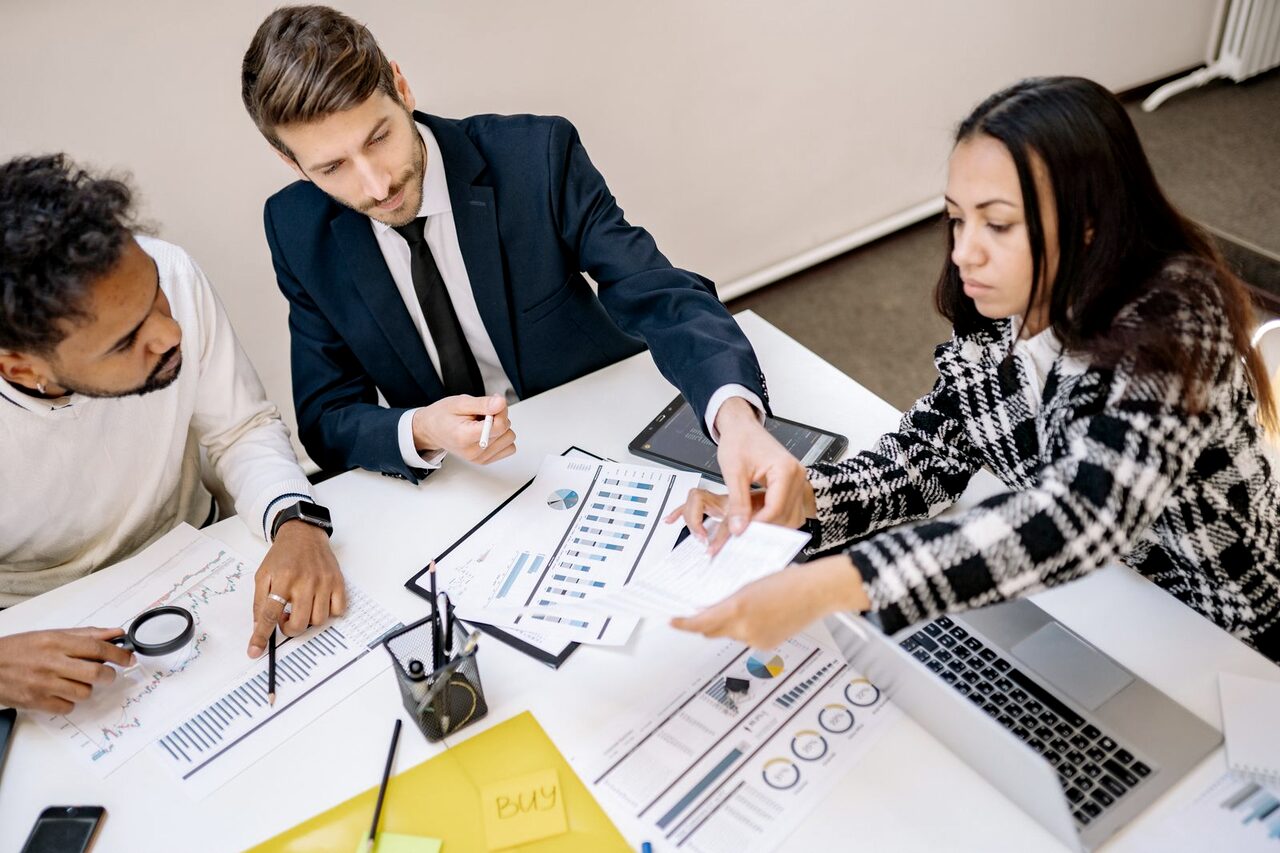 Two colleagues reviewing printed reports together across a meeting-room table.