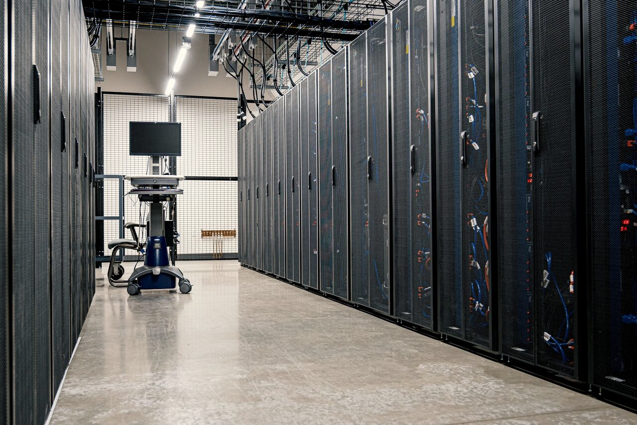 A long aisle of networking racks in a data centre, with a diagnostic cart part-way down it.