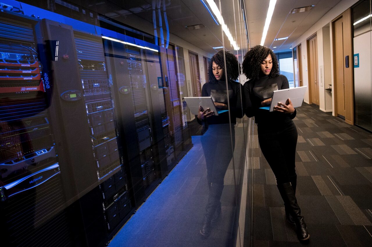 An engineer with a laptop walking a blue-lit aisle of servers.