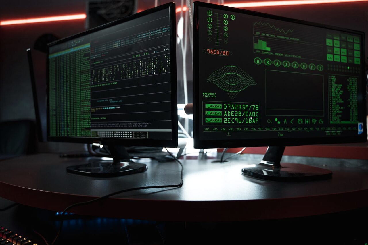 Lines of code and a terminal session glowing green across two monitors in a dark room.