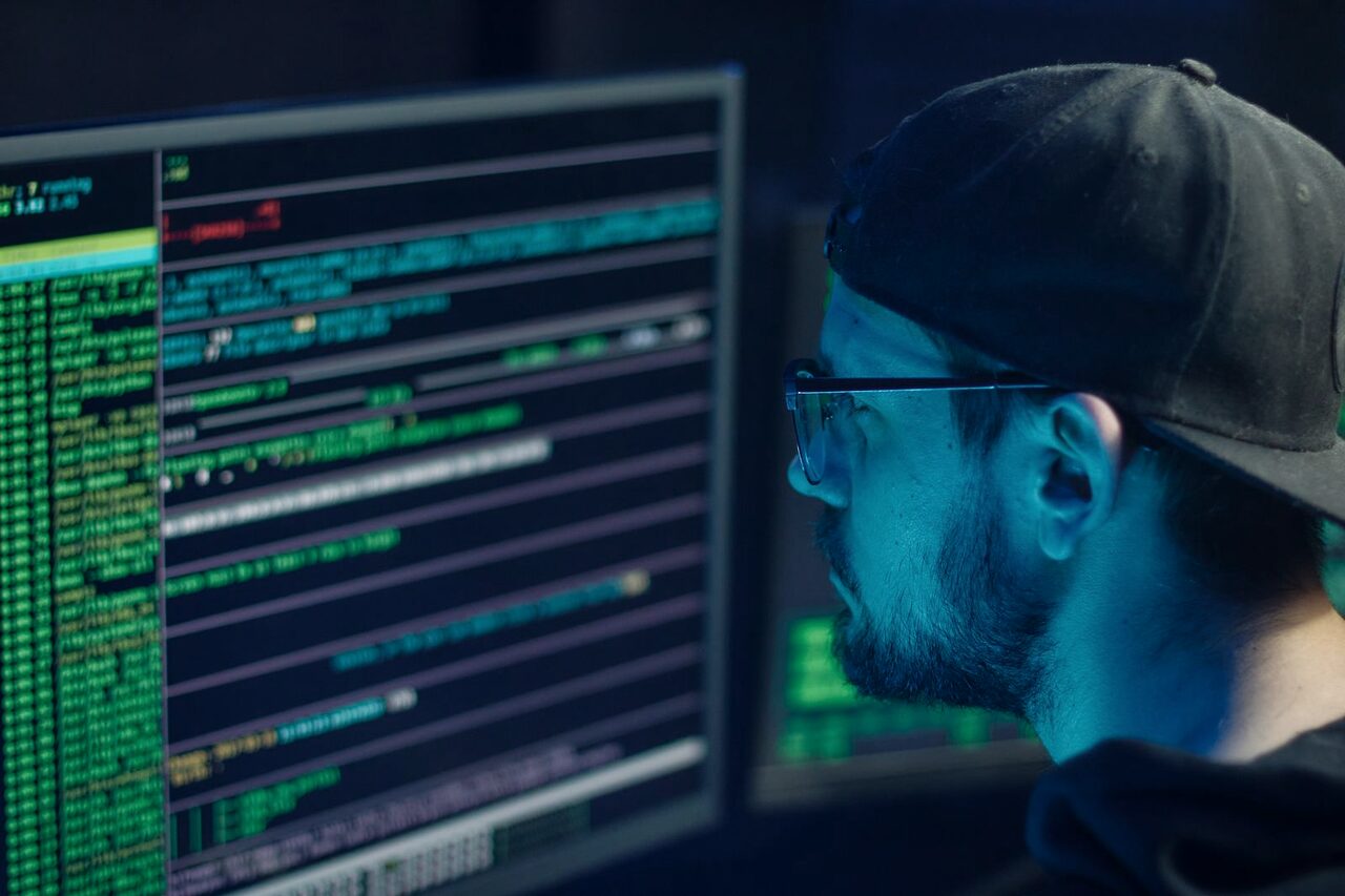 A security analyst studying streams of live log data on a monitor in a darkened operations room.