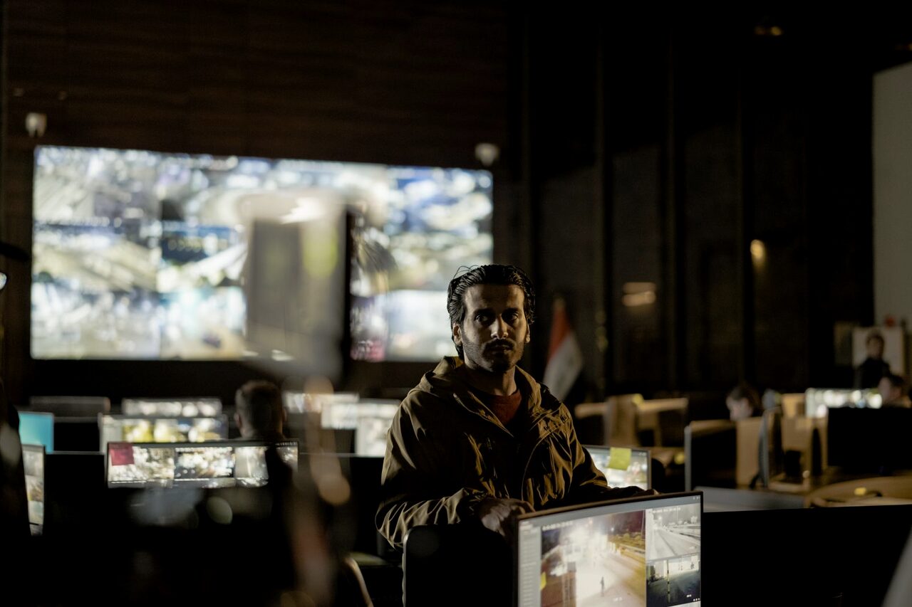 An analyst watching a bank of surveillance monitors in a dim security operations room.